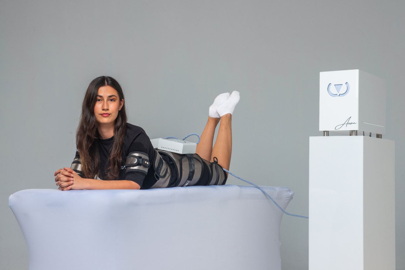 Client lying on a treatment bed with the Wonder bands on her legs; beside her, the Wonder Axon device on its stand
